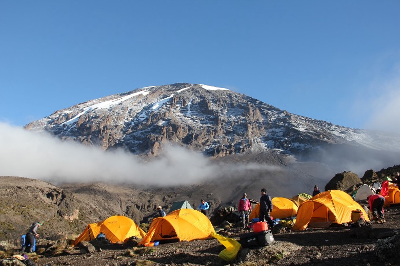 Trekkers resting at a Kilimanjaro campsite with tents and mountain backdrop.